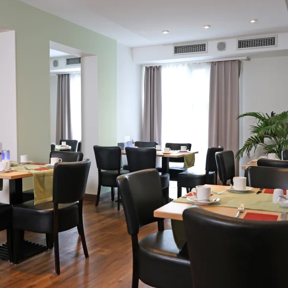 Raum mit kleinen Tischen, eingedeckt für Frühstück.